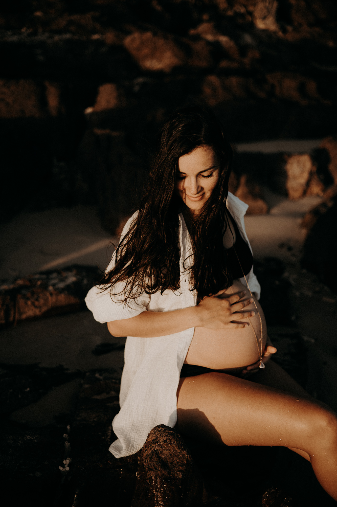 femme enceinte au ventre dénudée assise sur la plage au coucher du soleil